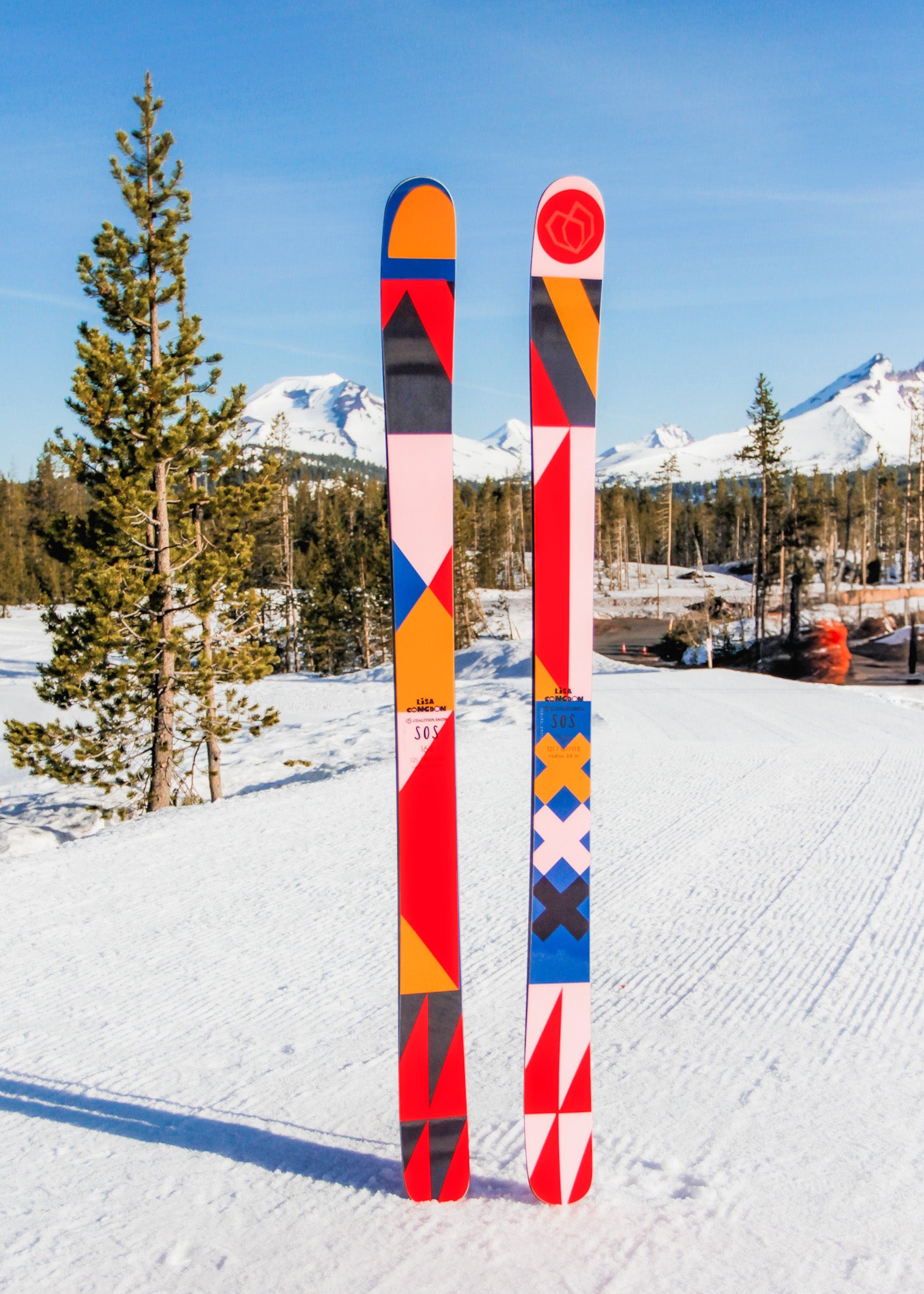 Colorful skis designed by Portland-based artist Lisa Congdon with geometric patterns on a snowy background with trees and mountains.