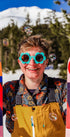 Person holding colorful skis with a mountain and trees in the background