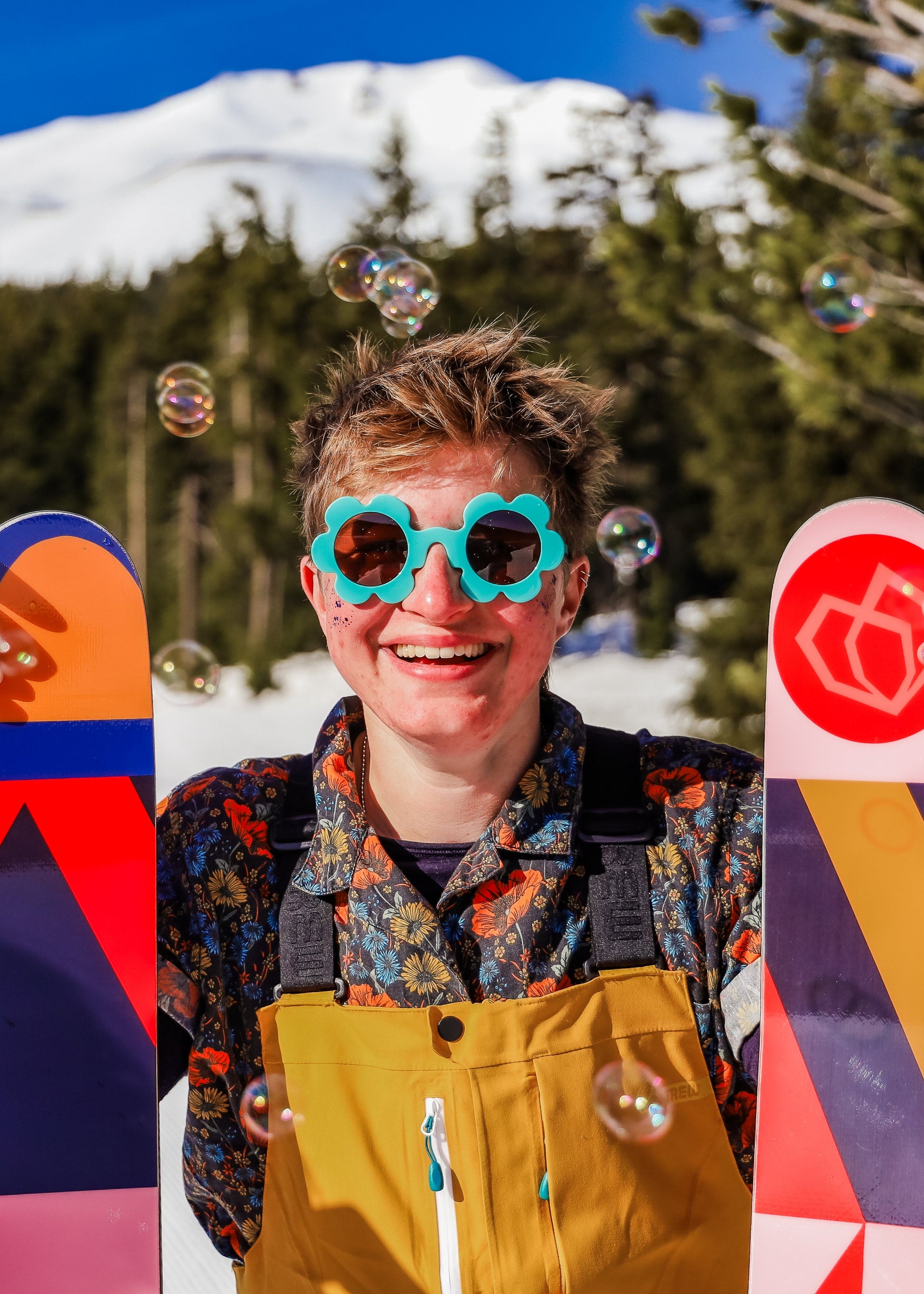 Person holding colorful skis with a mountain and trees in the background