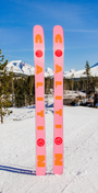 Pink and orange skis with a mountainous landscape in the background