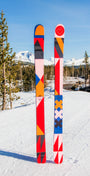 Colorful skis designed by Portland-based artist Lisa Congdon with geometric patterns on a snowy background with trees and mountains.