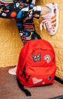 Person wearing colorful pants and shoes with a red backpack against a yellow textured wall featuring NoSo Patches.