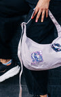 Person holding a light purple handbag with decorative NoSo Patches, wearing black pants and sneakers.