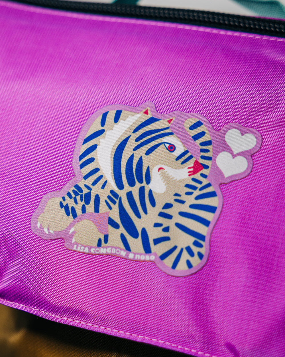 Purple bag with a Lisa Congdon tiger design patch and hearts on a pink background